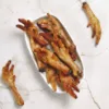 View of Wiggles N' Nibbles Chicken Feet dog treats showing dried chicken feet in a white dish with additional pieces on a light marble background.